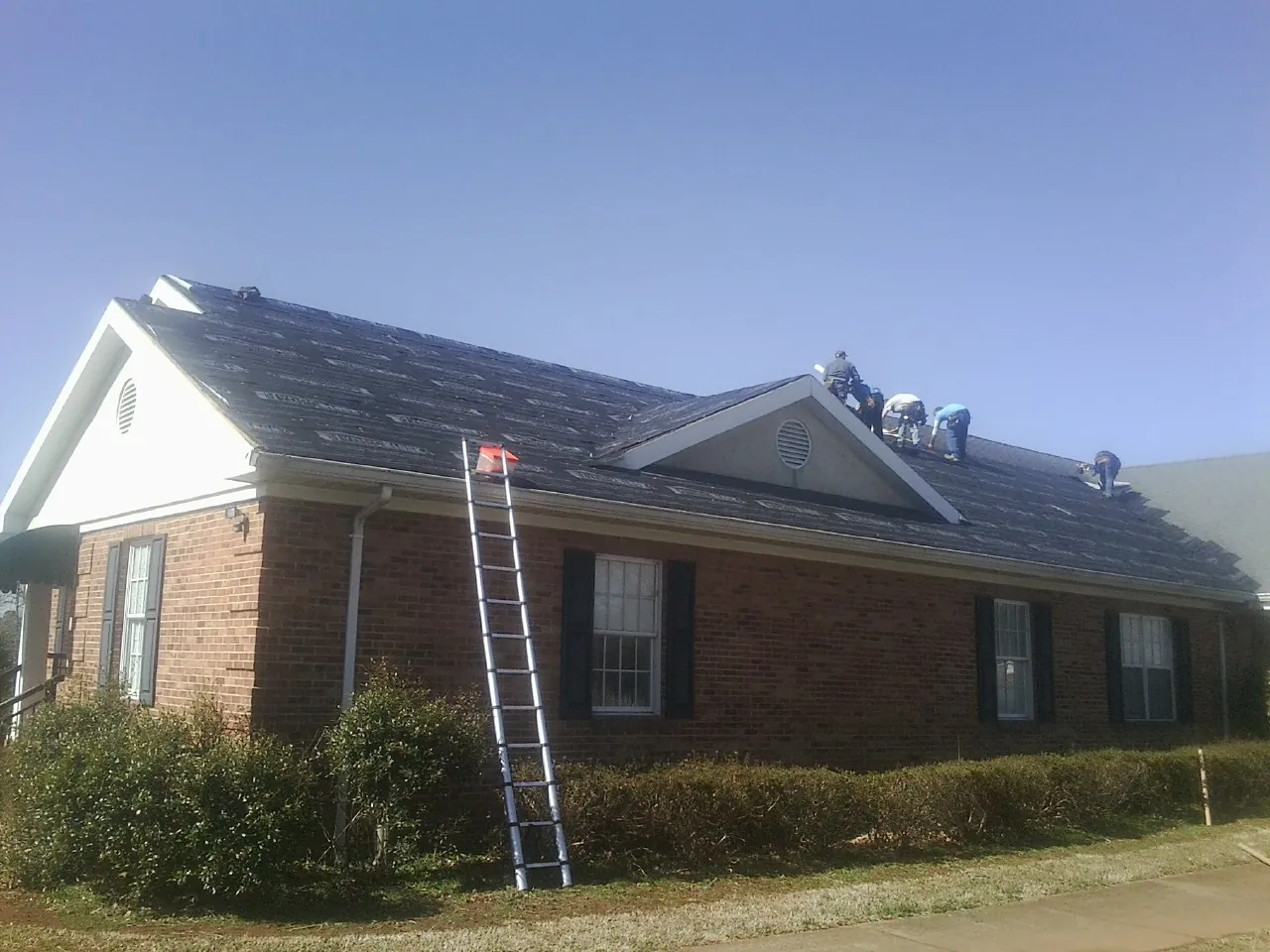 Crew tearing shingles off a brick ranch roof with a ladder set — Emergency Roof Repair work by our crew in Ripon