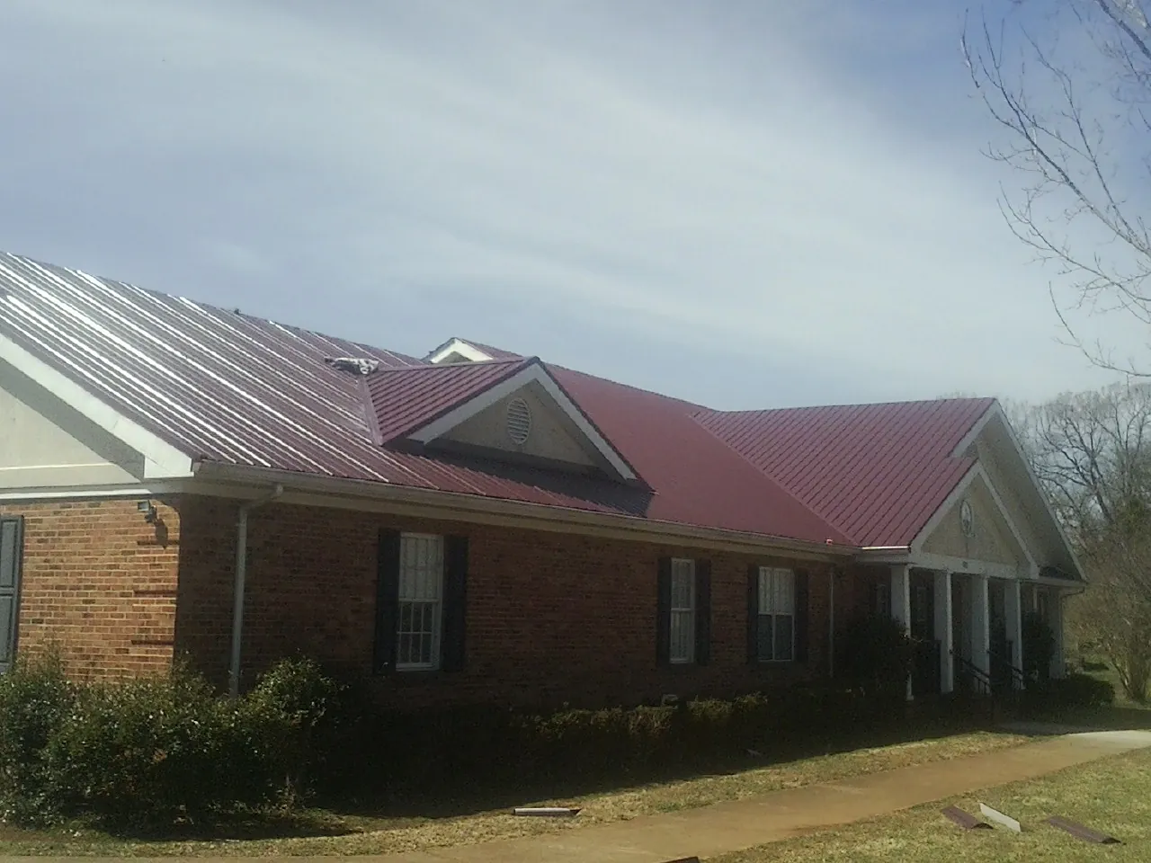 Red metal roof with gabled entries on a long brick building, from a Hail Damage Roof Repair job in Ripon