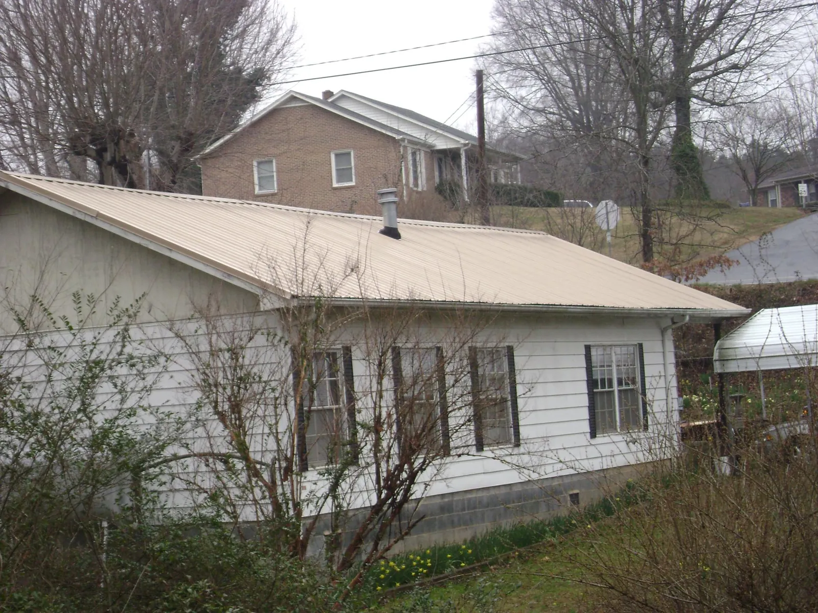 Tan metal roof on a white sided house set into a hillside — Commercial Roofing by Roofing Brothers in Ripon